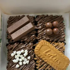 My four-piece assorted brownie box is perfect for sampling different flavors. This box includes KitKat, chocolate balls, white chocolate chip, and Lotus Biscoff toppings on my classic fudgy brownie base.