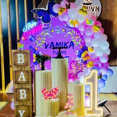 A vibrant butterfly theme for a first birthday, featuring a custom purple backdrop with the child's name. The setup includes a 'Happy Birthday' neon sign, a large light-up '1', 'BABY' blocks, and a pink and white balloon garland.