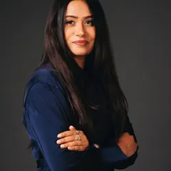 A strong and confident headshot for a professional woman. The crossed-arm pose and direct gaze project authority and trustworthiness. The dark, neutral background keeps it professional.