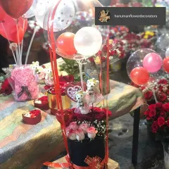 This celebration box is designed for pure fun and affection. It combines pink and red roses with adorable teddy bears and a cascade of festive red and white balloons, making it a wonderful surprise gift.