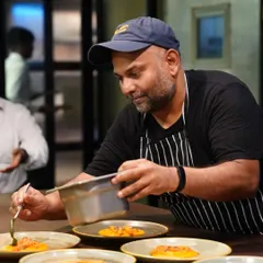 A chef in the middle of service, carefully plating multiple dishes with intense focus. This candid shot captures the high-energy environment and dedication of a professional kitchen.