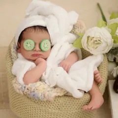 A hilarious and adorable spa day setup, with a newborn in a tiny white bathrobe and cucumber slices on their eyes.