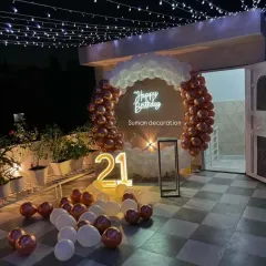 A chic 21st birthday party setup on a rooftop terrace. I used a circular balloon arch with rose gold and white balloons, a neon sign, and a light-up number to create a festive night-time vibe.