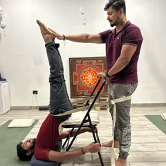 This is a supported shoulder stand, or Sarvangasana, using a chair and belts. This therapeutic setup ensures correct alignment, decompresses the spine, and allows the practitioner to receive the full benefits of the inversion safely. In my training, you will master the art of using props to make yoga accessible and beneficial for every body.