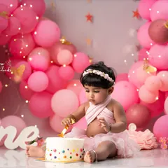 The moment of discovery during a first birthday cake smash. This shot captures the pure joy and curiosity as she touches her custom-made cake for the first time, surrounded by a beautiful pink balloon arch.