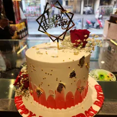 A chic and celebratory birthday cake. This design combines a red watercolor effect with gold leaf accents, fresh flowers, and a modern geometric 'Happy Birthday' topper.