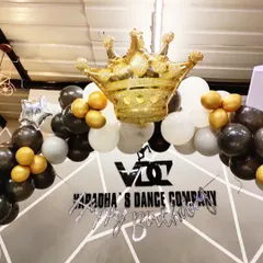 A close-up of the balloon arrangement for the studio event. The black, white, and gold balloons are topped with a large, inflatable gold crown, perfectly matching the celebratory and regal theme.