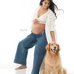 A relaxed and modern maternity portrait. The mother-to-be shares a happy moment with her golden retriever, showcasing a casual and authentic family bond.
