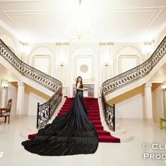 A breathtaking wide shot of a bride in a magnificent black gown with a long train, standing on the grand staircase of a palace-like studio set.