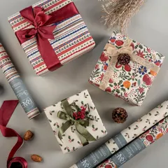 A festive flat lay of beautifully wrapped Christmas gifts using Rae's wrapping paper. The composition includes rolls of paper and natural elements like pinecones, creating a warm and inspiring holiday gifting scene.