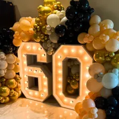Celebrating a 60th birthday in style with giant, 4-foot tall marquee numbers. The numbers are framed by a dense balloon garland in a classic black, gold, and white color scheme for a timeless look.