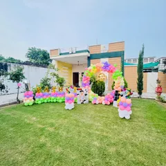 A magical unicorn-themed birthday party in an outdoor garden setting. The setup includes a rainbow balloon arch, unicorn cutouts, and foil balloons spelling out the birthday girl's name, "Kashvi."