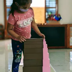Deep concentration is a hallmark of Montessori learning. This child is fully engaged with the Pink Tower and Broad Stair, classic sensorial materials that help develop visual discrimination of size and dimension.