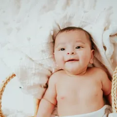 A happy four-month-old smiling from his cozy basket. Milestone sessions are perfect for capturing their budding personality as they learn to smile and interact with the world.