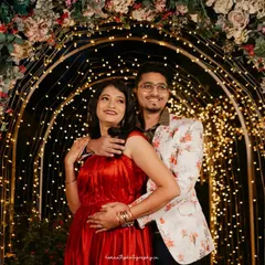 A couple poses under a beautifully decorated arch of flowers and fairy lights at night, creating a magical and romantic atmosphere.