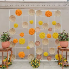A creative and rustic photo backdrop for a Haldi ceremony. We used a simple white grid decorated with woven baskets and spheres of yellow and orange marigolds for a unique, textured look.
