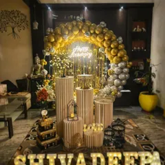An elegant anniversary setup in a living room, featuring a gold and silver balloon arch, a 'Happy Anniversary' neon sign, and my signature prop display.