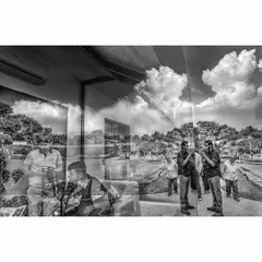 A black and white version of the gallery reflection. Stripping away the color emphasizes the forms, the clouds, and the ghostly figures, creating a more graphic and surreal composition of layered realities.