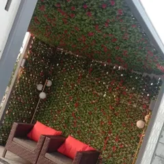 Another example of an outdoor seating nook created with a trellis covered in artificial leaves and red flowers. The greenery provides privacy and a vibrant, garden-like atmosphere for this cozy corner.