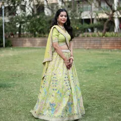 A full shot of the client in the lime green peacock lehenga, looking elegant in a garden setting.