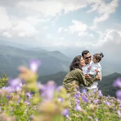 A breathtaking wide shot of the family on a mountaintop, with the Neelakurinji flowers in the foreground. This photo captures both the intimate family moment and the grand, beautiful landscape.