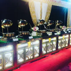 An elegant buffet arrangement for an engagement ceremony, featuring illuminated counters and polished golden chafing dishes. The setup is designed for both beauty and efficient guest flow.