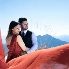 An intimate embrace against the backdrop of snow-capped mountains. The flowing red fabric adds a touch of drama and movement, creating a powerful image that is both romantic and visually striking.