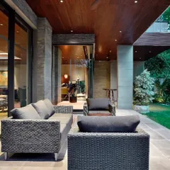 A covered outdoor seating area in a Gurgaon residence, seamlessly connected to the indoor living space. The wooden ceiling and stone flooring extend outwards, blurring the line between the home and the garden.