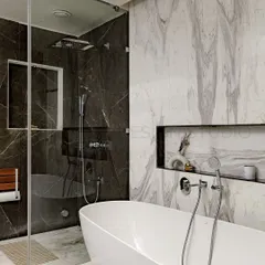 This modern bathroom is a masterpiece of architectural ingenuity. The contrast between the dark and light marble, the freestanding tub, and the glass-enclosed shower creates a sense of luxury and royal sophistication.