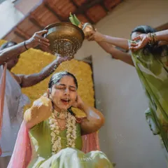 A traditional moment during a Haldi ceremony. The bride is showered with holy water against a backdrop made entirely of bright yellow marigolds, a classic and auspicious choice for this event.