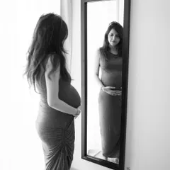 A moment of reflection. Seeing your changing body in the mirror is a powerful part of the pregnancy journey, captured here in a thoughtful black and white portrait.