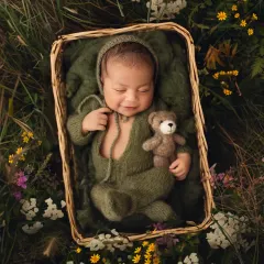 A sweet newborn boy in an olive green romper, nestled in a basket in a field of digital wildflowers. This composite image shows how I can create outdoor looks in a controlled studio environment.
