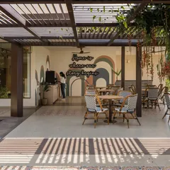 The outdoor cafe at Brigade Valencia is designed as a series of verandahs and courtyards. The space is adorned with patterned tiles and a playful mural, creating a relaxed and vibrant atmosphere.