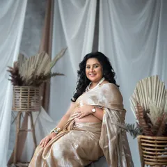 A beautiful seated portrait that highlights the intricate details of the saree and the radiant smile of the mother-to-be.