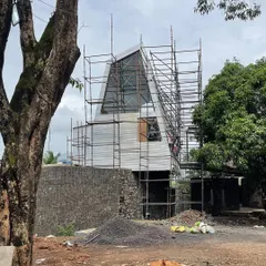 The Karjat residence enveloped in scaffolding, revealing its complex, angular geometry. Even in this raw state, the structure's dynamic relationship with the surrounding trees and landscape is evident.