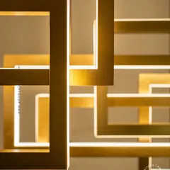 A multi-layered chandelier composed of intersecting rectangular frames with a brushed gold finish. The integrated LEDs cast a warm, ambient light, creating a dynamic and architectural statement piece for modern interiors.