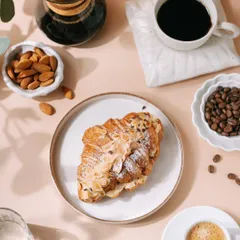 A flatlay of an almond croissant surrounded by coffee beans, a Chemex, and almonds. This composition tells a story of a complete coffee and pastry experience, perfect for a bakery's promotional content.