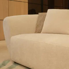 A close-up of the clean lines and gentle curves of one of our custom sofas. Upholstered in a soft, off-white fabric with a contrasting textured cushion, this piece highlights our focus on subtle details and high-quality finishes for modern living.