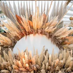 A stunning example of a boho-chic theme, featuring a massive sun-like backdrop made entirely of pampas grass. This design element creates a dramatic yet earthy focal point, perfect for a rustic and romantic sangeet or cocktail evening.