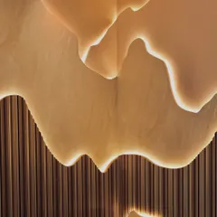 A close-up of the custom-designed, back-lit wall feature. The soft glow emphasizes the organic, layered forms and the texture of the fluted paneling below, creating a piece that is both architecture and art.