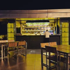 The main bar area of the rooftop cafe, featuring back-lit shelves that make the glassware sparkle. The warm, yellow-toned lighting creates a focal point and an inviting glow.