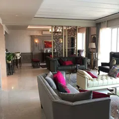 This living space is designed as an amalgamation of styles, blending classic comfort with contemporary details. The open-plan layout is defined by a geometric screen partition, creating distinct zones for lounging and a home bar while maintaining a cohesive flow.