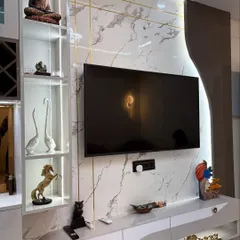 This TV unit features a white marble-finish back panel with elegant gold inlay work. The design includes open shelves for displaying decor, like the Buddha statue, and closed cabinets for clutter-free storage.