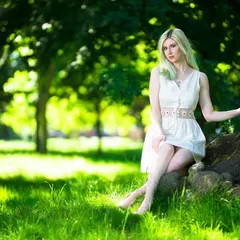 A full-body portrait from the same London park shoot. The composition uses the tree trunk as a natural prop, and the soft, dappled sunlight creates a beautiful texture on the grass and a gentle light on the model.