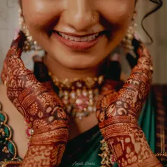 The beautiful smile of a happy bride, with her hands framing her face to show the stunningly dark henna stain.