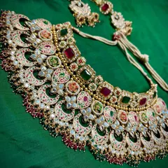 Red for love, green for new beginnings. This complete bridal set tells a story with its colorful Meenakari work, featuring a statement necklace and matching maang tikka.