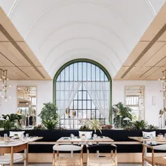 The main dining hall at Brassa is designed to feel bright, airy, and connected to the outdoors. The grand barrel-vaulted ceiling and large arched window create a sense of scale, while lush greenery and natural materials make the space feel welcoming and serene.