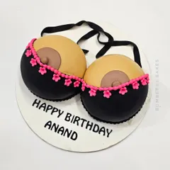 A "Happy Birthday Anand" cake with a playful, adult theme, featuring a sculpted bra.
