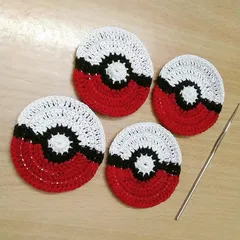 A set of four handmade crochet Pokeball coasters, shown with the crochet hook used to make them. They are a fun, nostalgic, and practical accessory for any gamer or 90s kid.