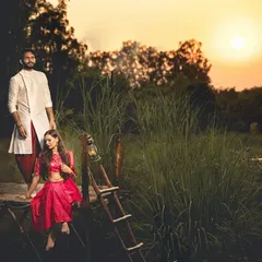 A stunning sunset shot of a couple in traditional attire, posed on a rustic wooden platform surrounded by tall grass.